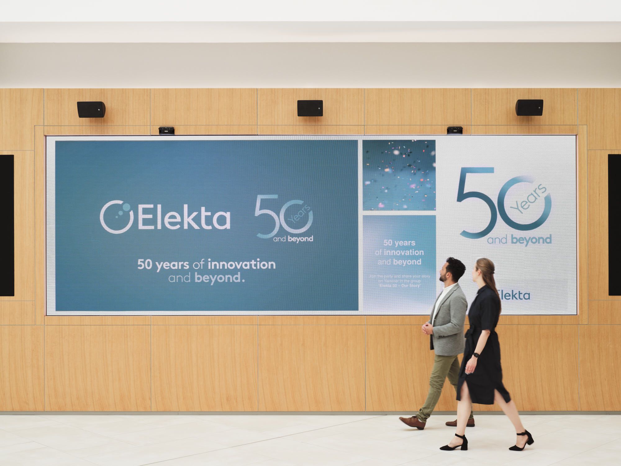 Two people walking in front of the Elekta Board Room screen.